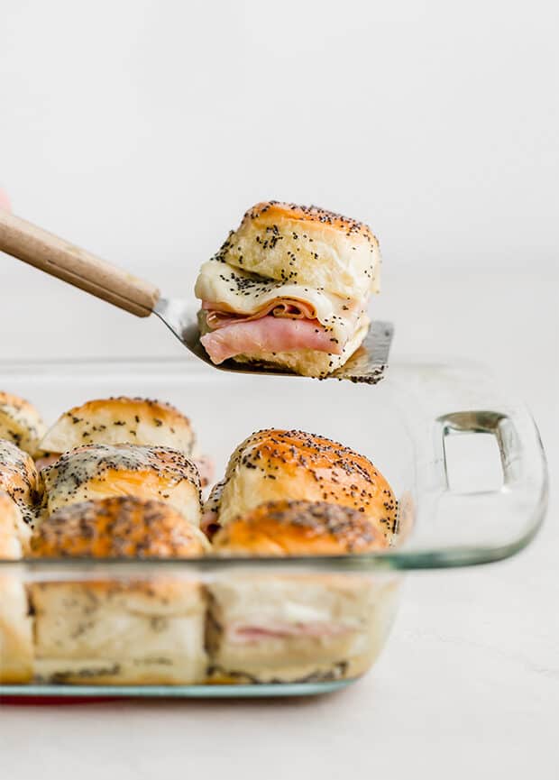 A spatula holding up a baked ham and cheese slider.