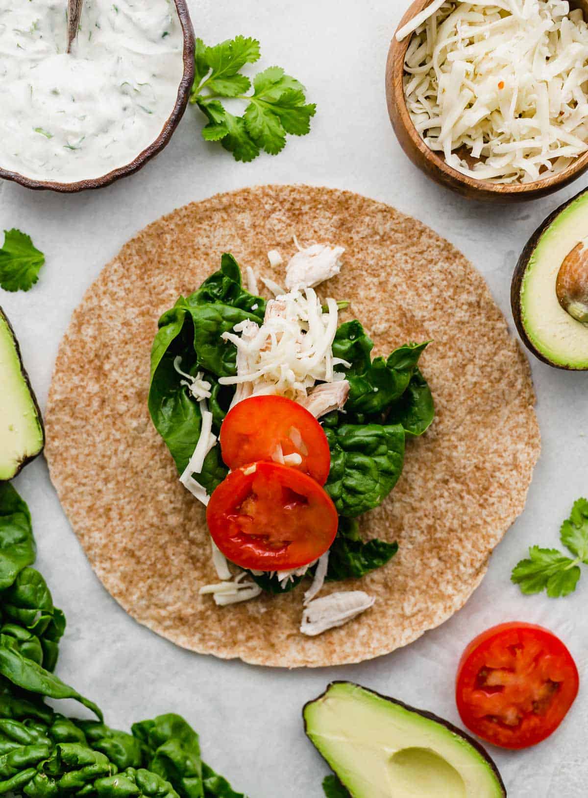 A whole wheat tortilla topped with rotisserie chicken, spinach, and sliced tomatoes.