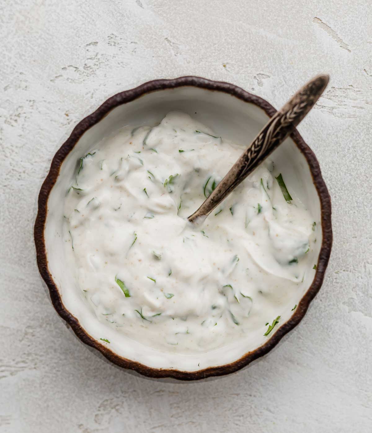 A cilantro lime greek yogurt mixture in a black rimmed white bowl.