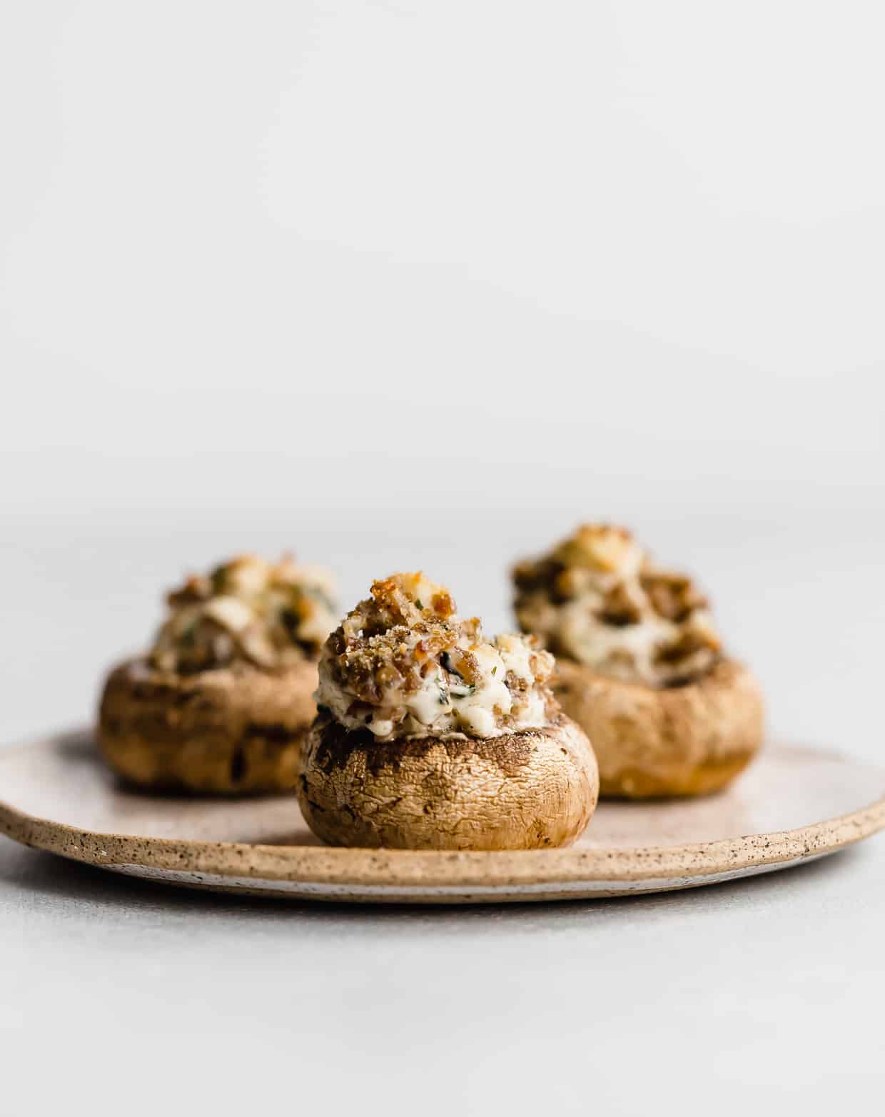 Italian Sausage Stuffed Mushrooms topped with bread crumbs, on a plate against a white background.