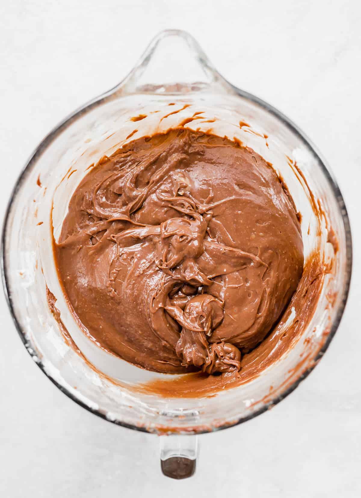 A creamy Nutella Cheesecake filling in a glass mixing bowl on a white background.