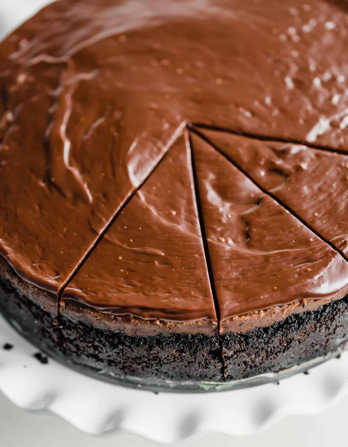 A nutella ganache topped Nutella Cheesecake baked on an Oreo crust, with several slices cut into the cheesecake.