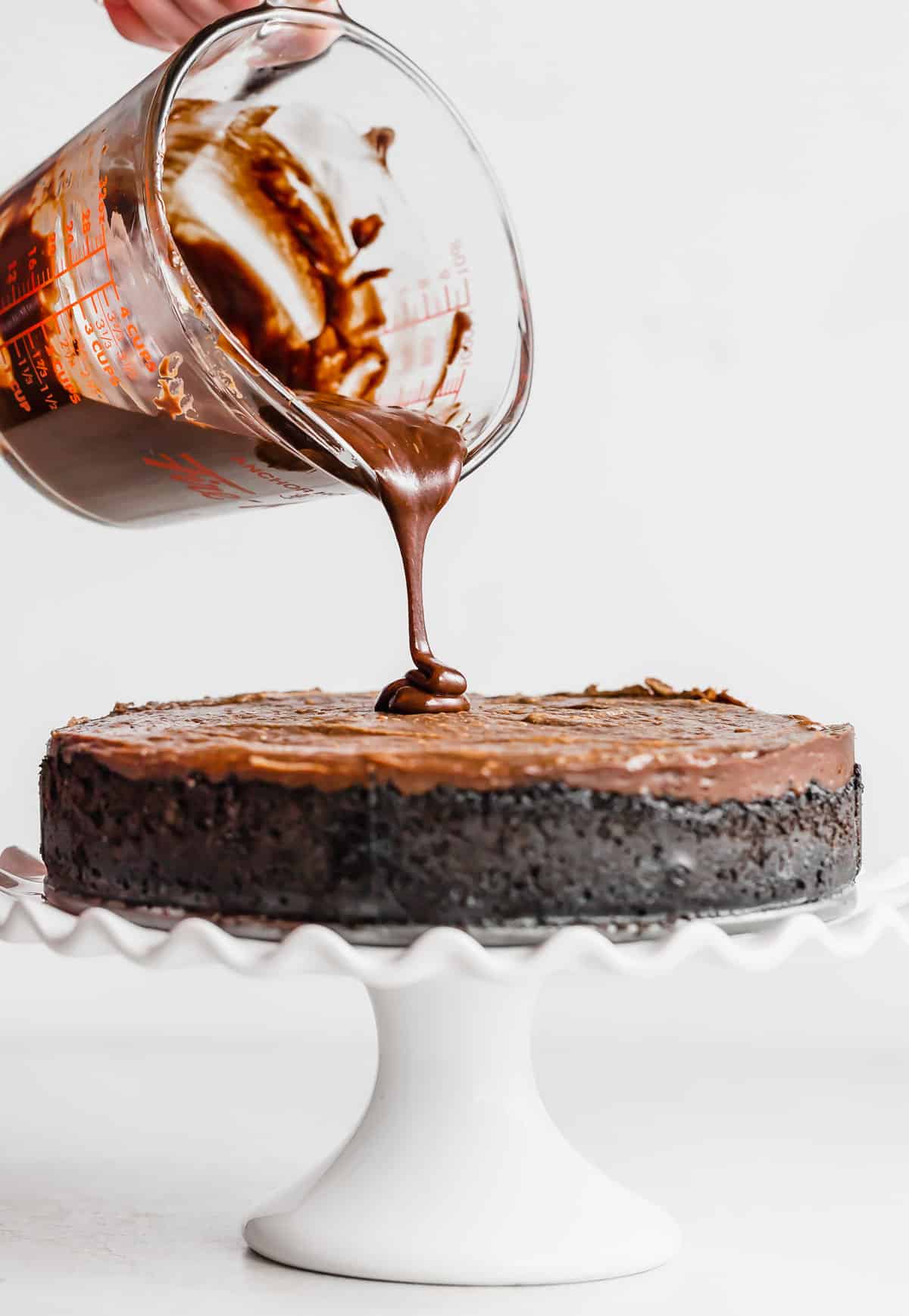 Nutella ganache being poured overtop a Nutella Cheesecake on a white cake stand.