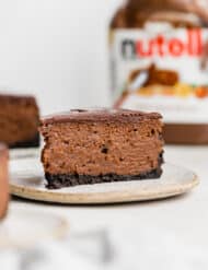 A slice of Nutella Cheesecake on a plate with a Nutella container in the background.
