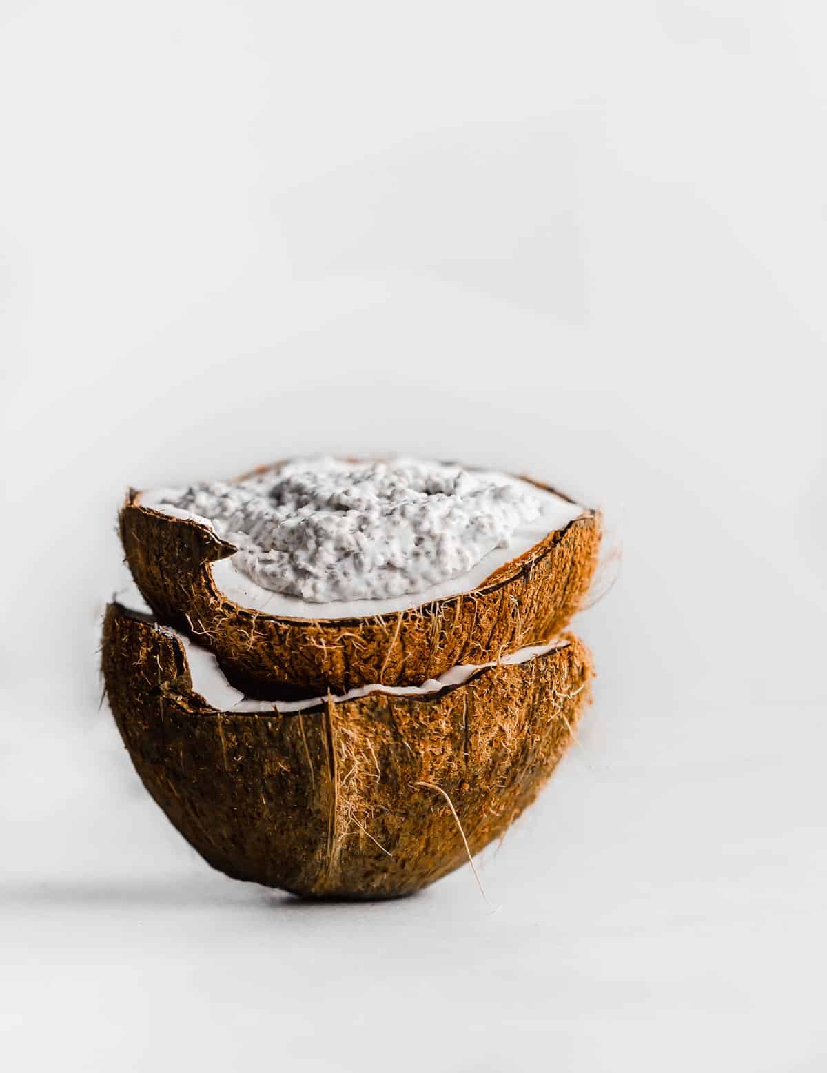 A raw coconut filled with Overnight Coconut Chia Pudding against a white background.