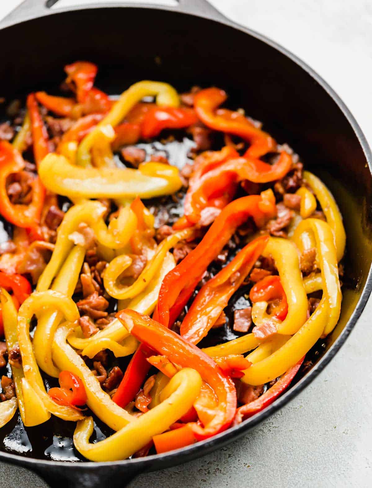 Sliced red and yellow peppers with prosciutto in a skillet.