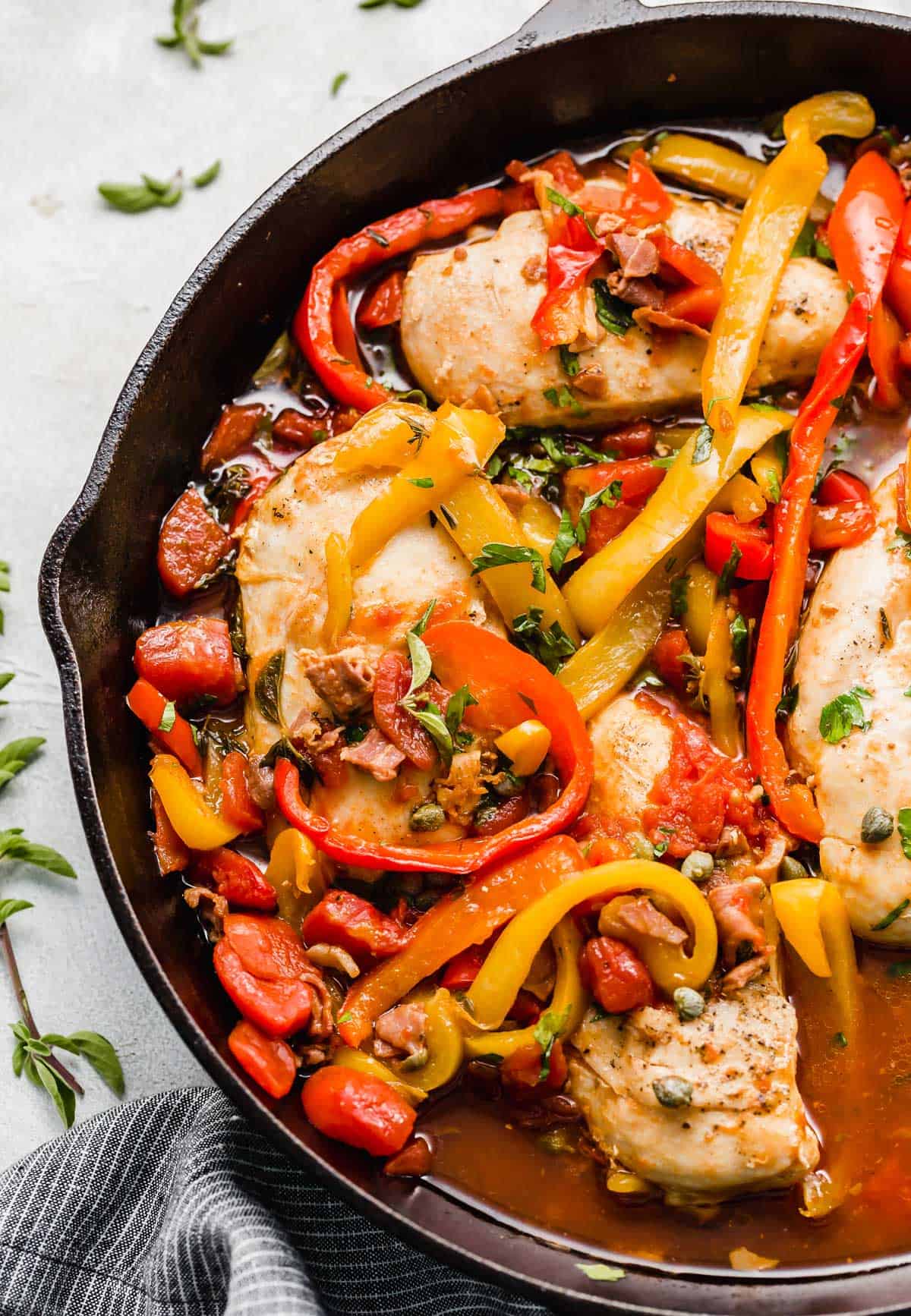 Skillet Roman Chicken recipe in a black skillet with sliced red and yellow peppers, fresh herbs, and capers.
