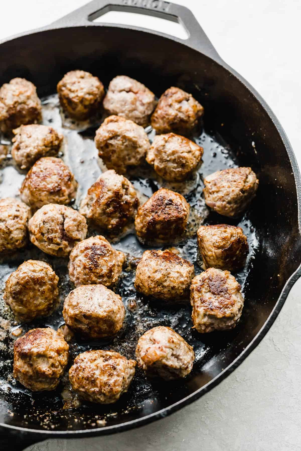 A black skillet with browned meatballs in it.