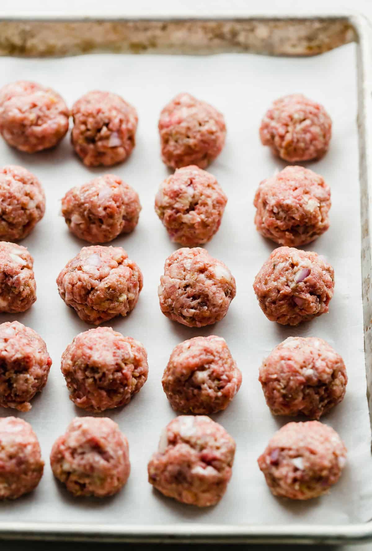 Raw Swedish Meatballs lined up in straight rows on a parchment lined baking sheet.