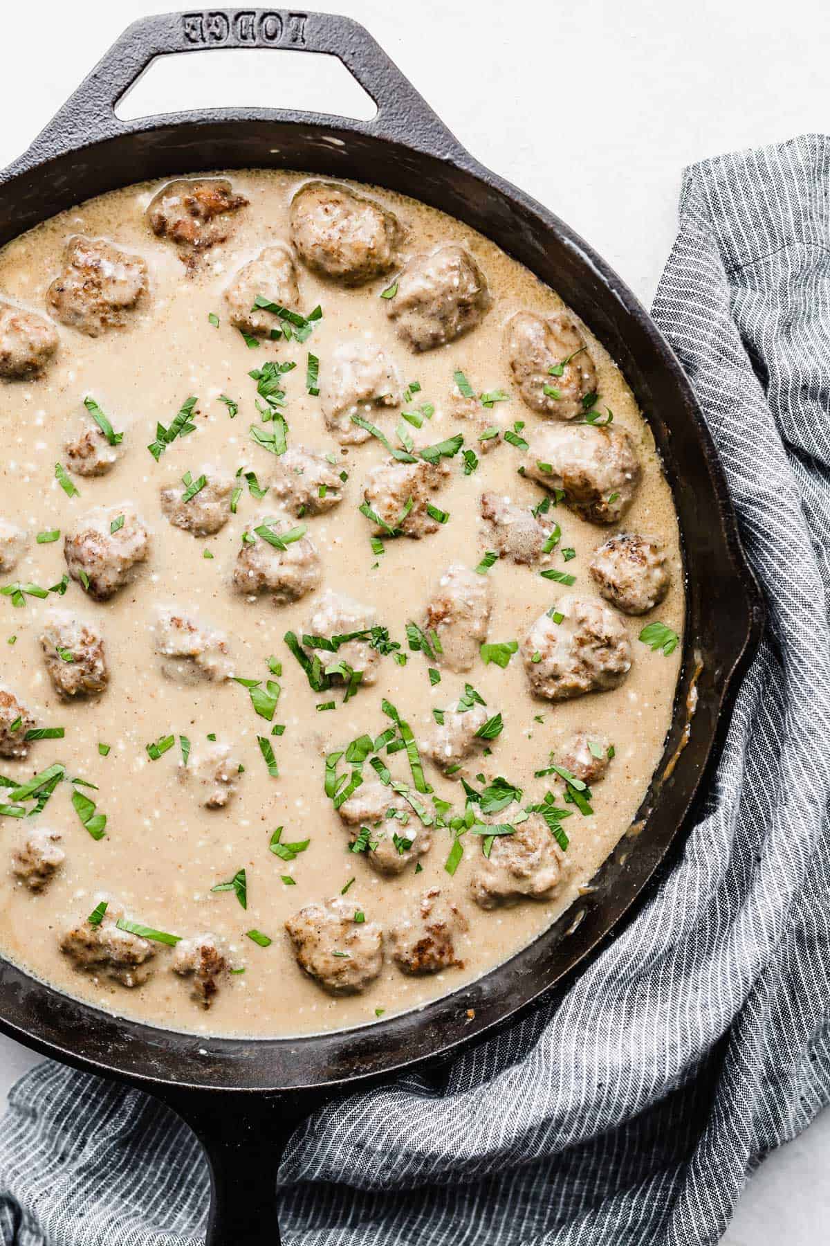 A skillet full of Swedish Meatballs and tan colored sauce on a white background.
