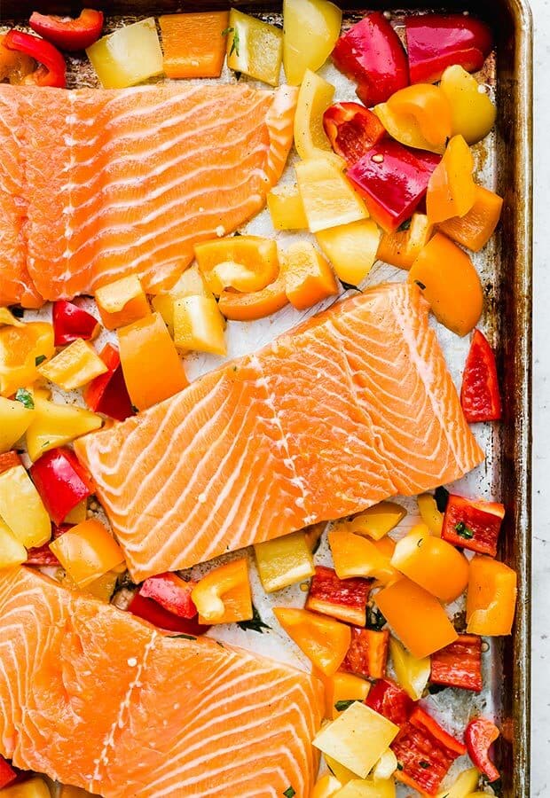 Unbaked salmon on a baking sheet surrounded by orange, yellow, and red chopped bell peppers.