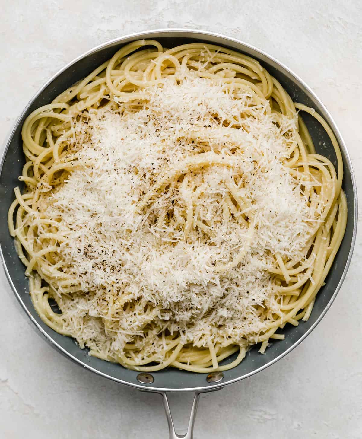 A gray skillet full of bucatini noodles topped with fresh parmesan cheese.