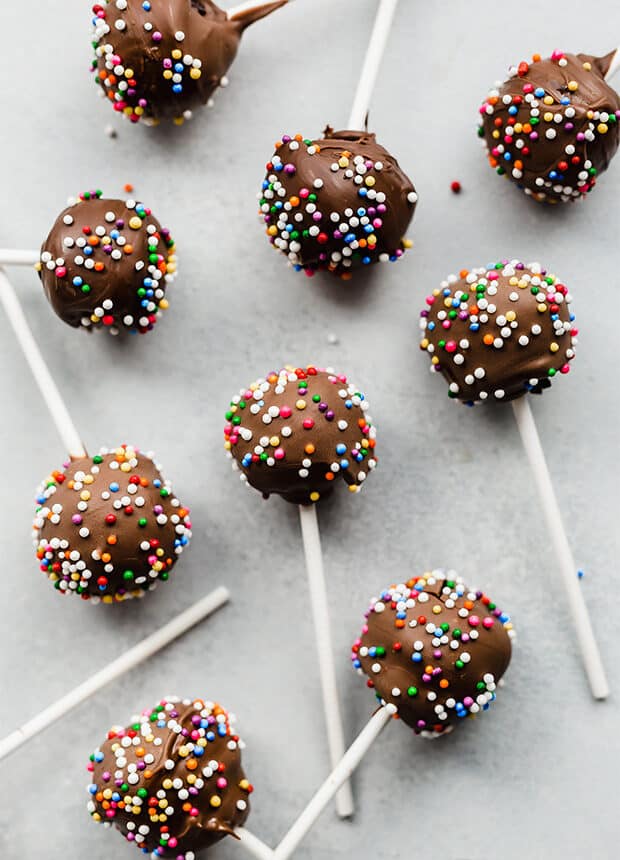 Sprinkle covered chocolate cake pops on a gray background.