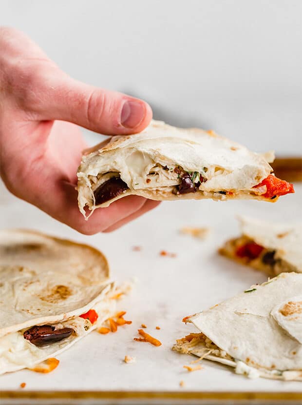A hand holding up a freshly baked Greek Quesadilla.