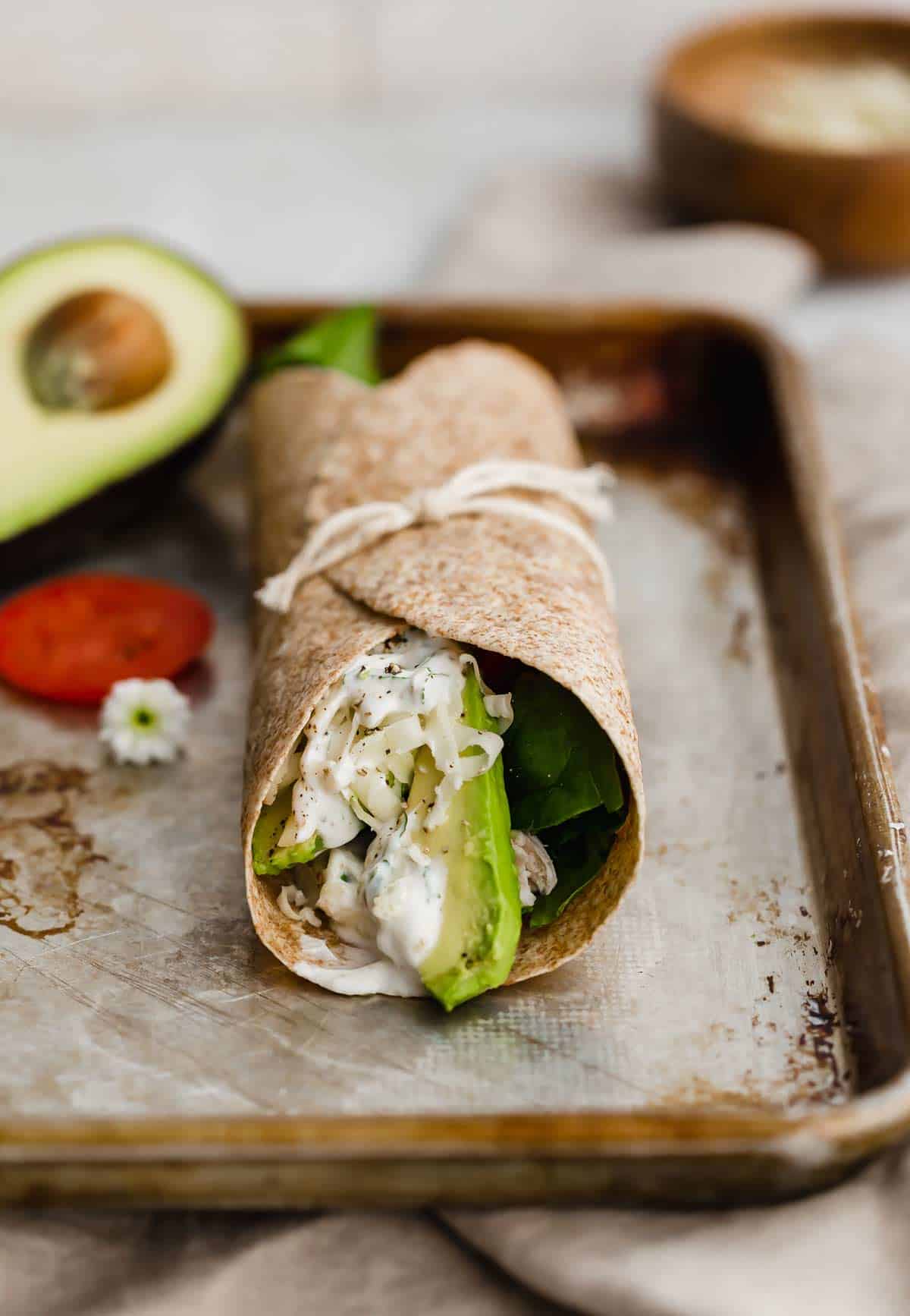 A whole wheat tortilla chicken wrap tied with a string, on a baking sheet.