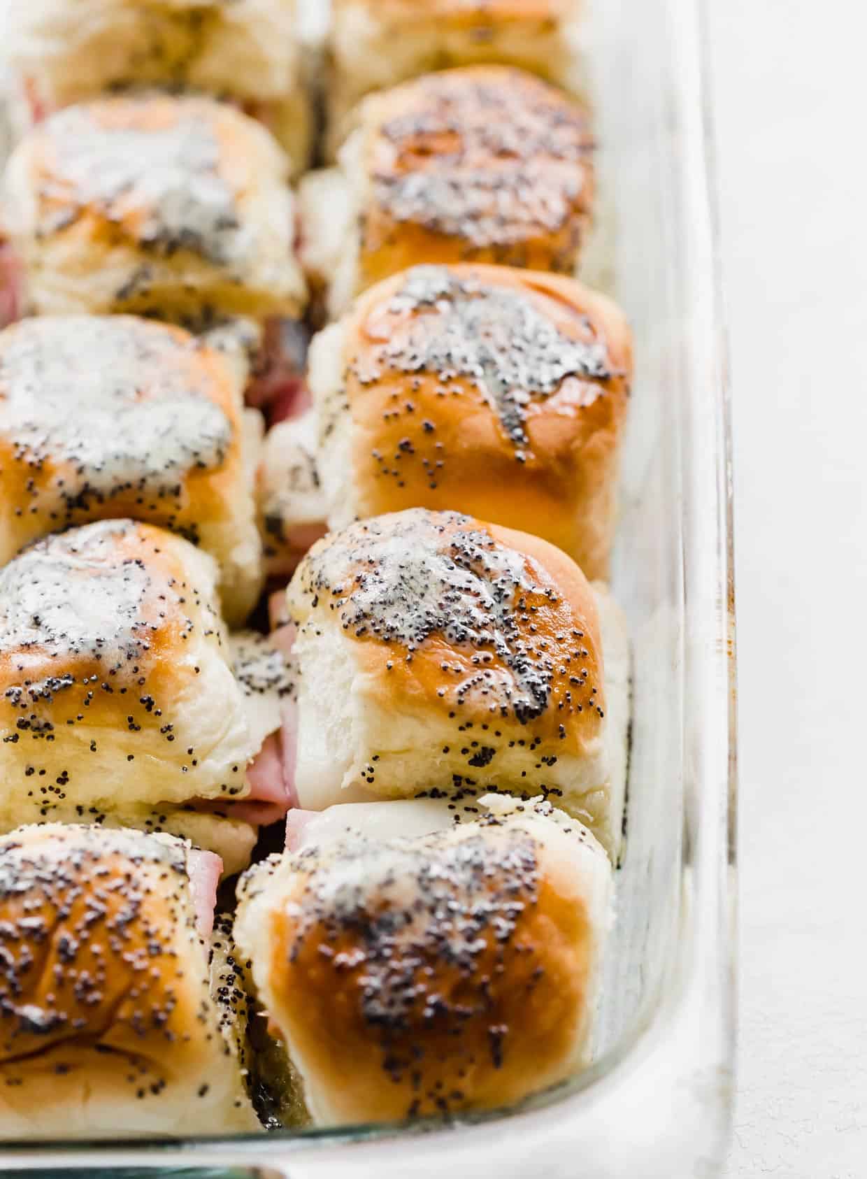 Honey Mustard Ham and Cheese Sliders made with Worcestershire sauce topped with a poppy seed dressing in a glass baking dish.