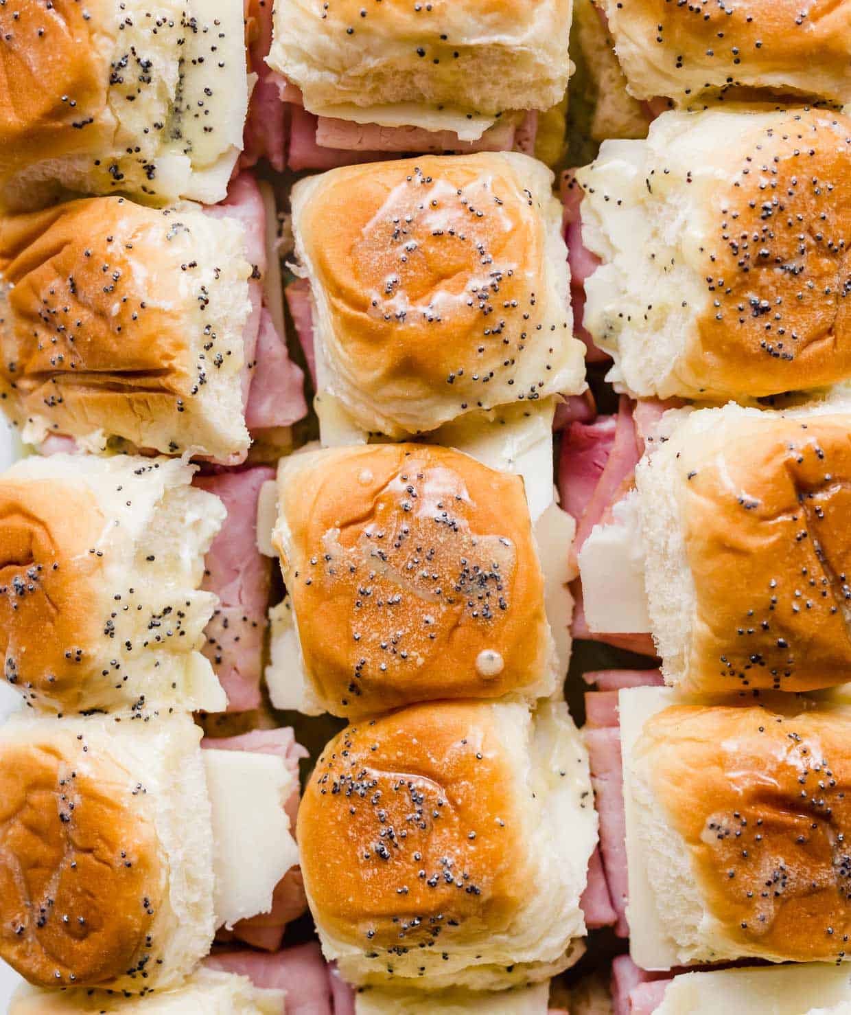 Overhead photo of Honey Mustard Ham and Cheese Sliders topped with a poppy seed dressing.