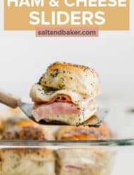 A spatula holding up a ham and cheese slider topped with a poppy seed dressing.