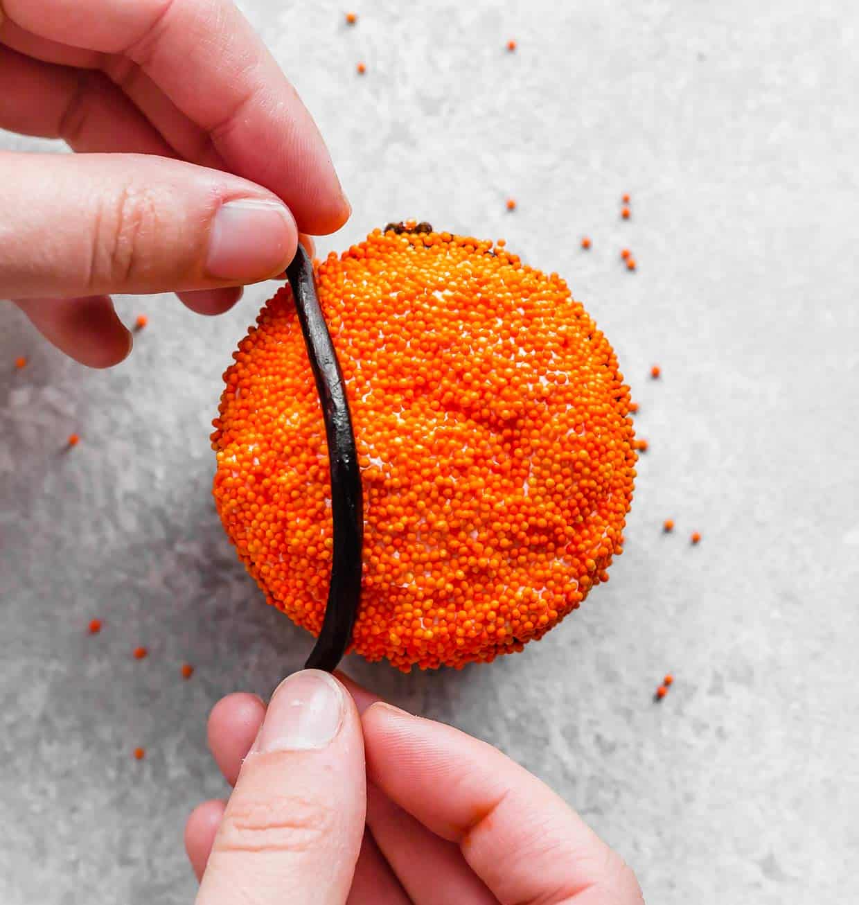 A hand placing a black licorice on a orange sprinkled cupcake.