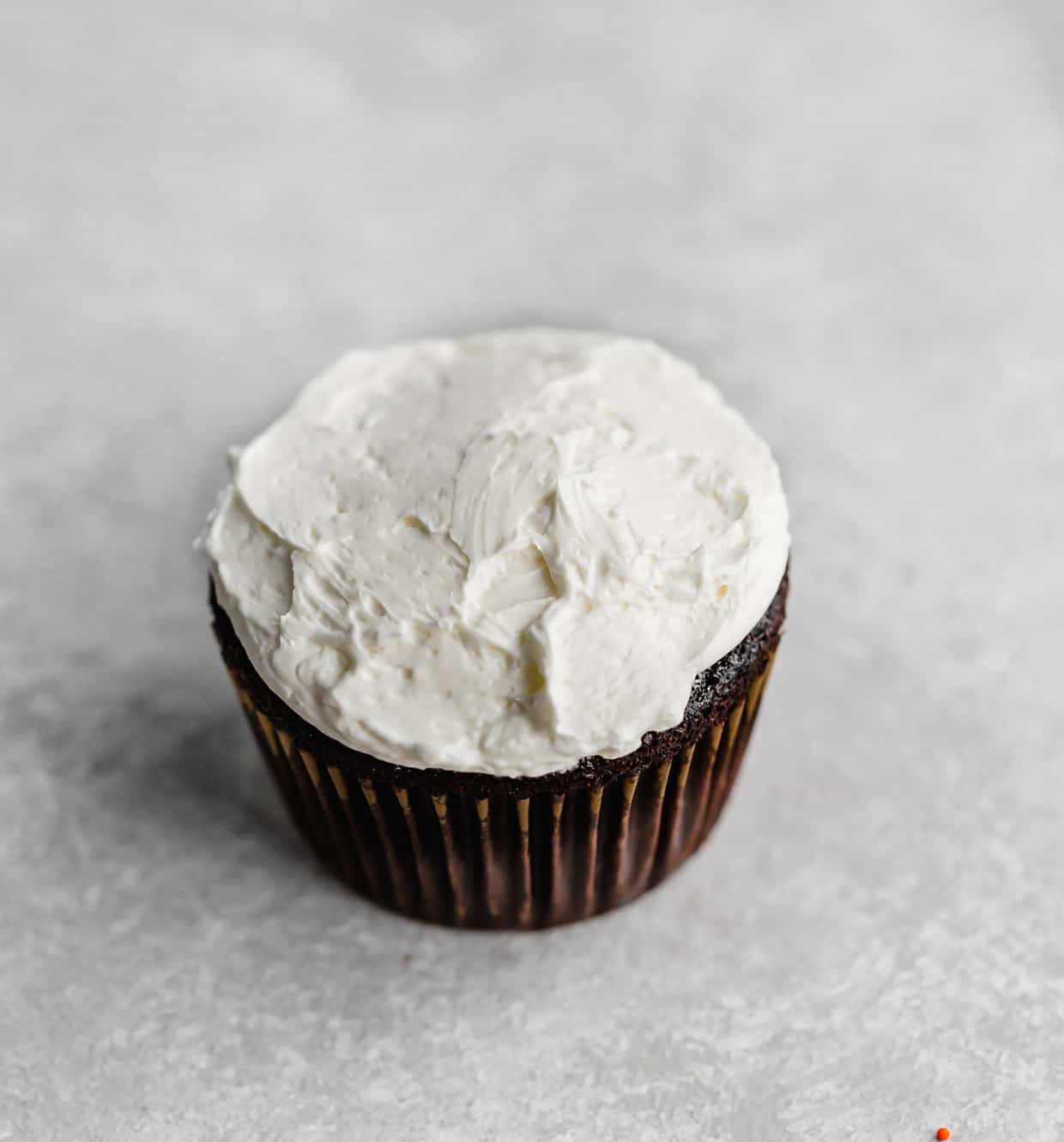 A swiss meringue buttercream frosted chocolate cupcake on a grey background.