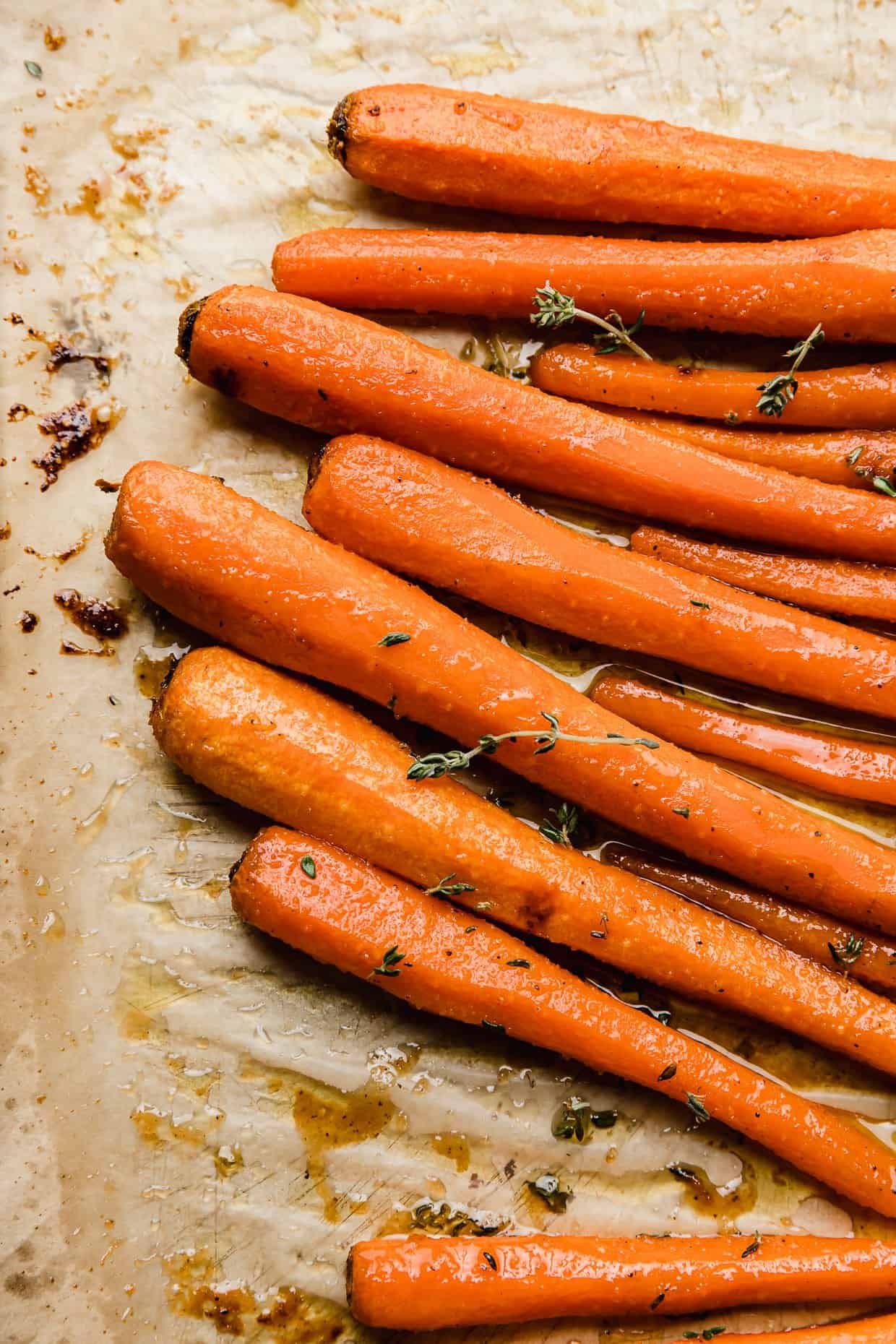 Brown Sugar Roasted Carrots with thyme on a tan parchment paper. 