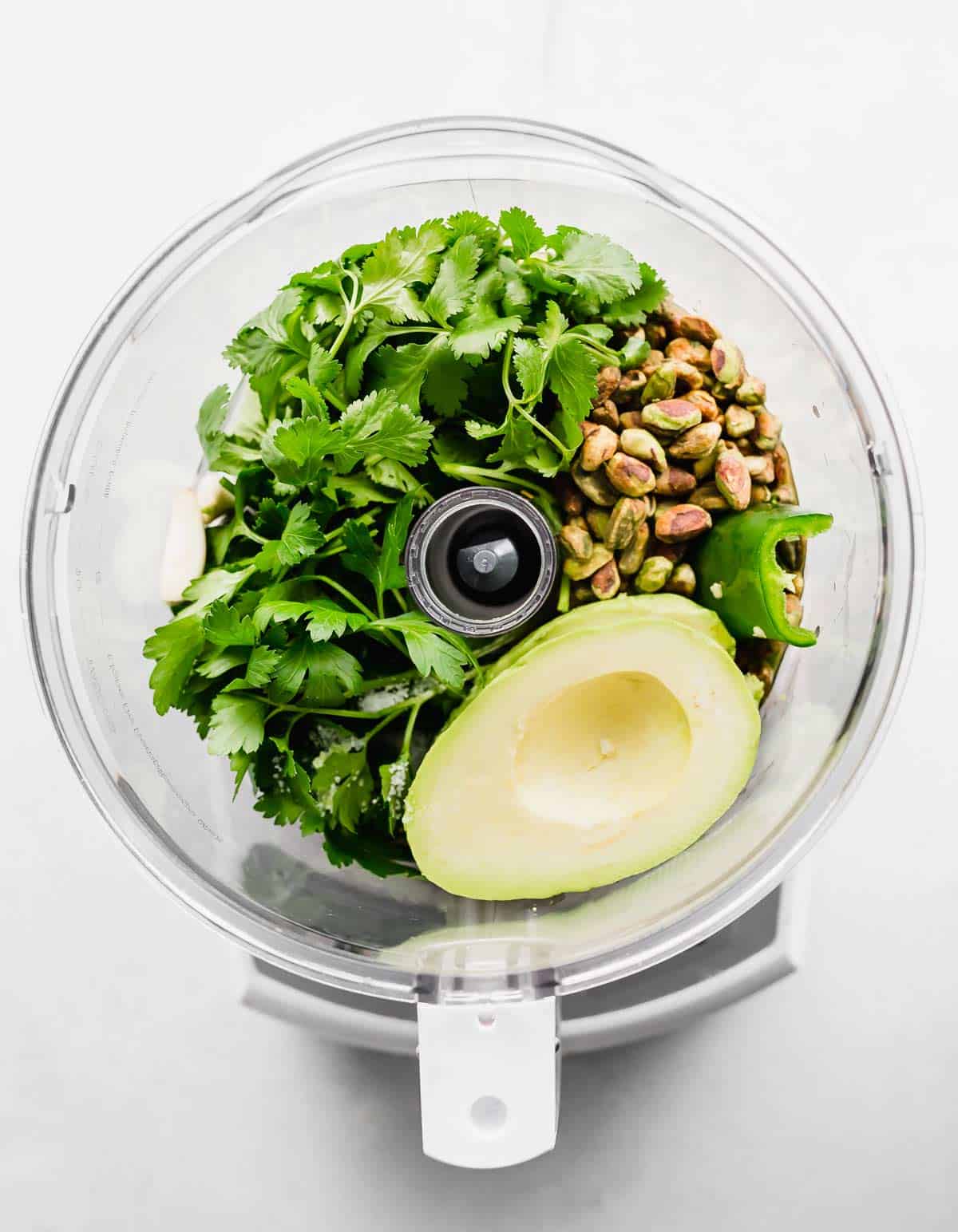 Green Sauce ingredients in a food processor, on a white background.