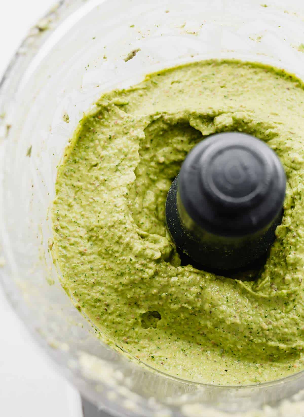 An avocado and herb green sauce in a food processor.