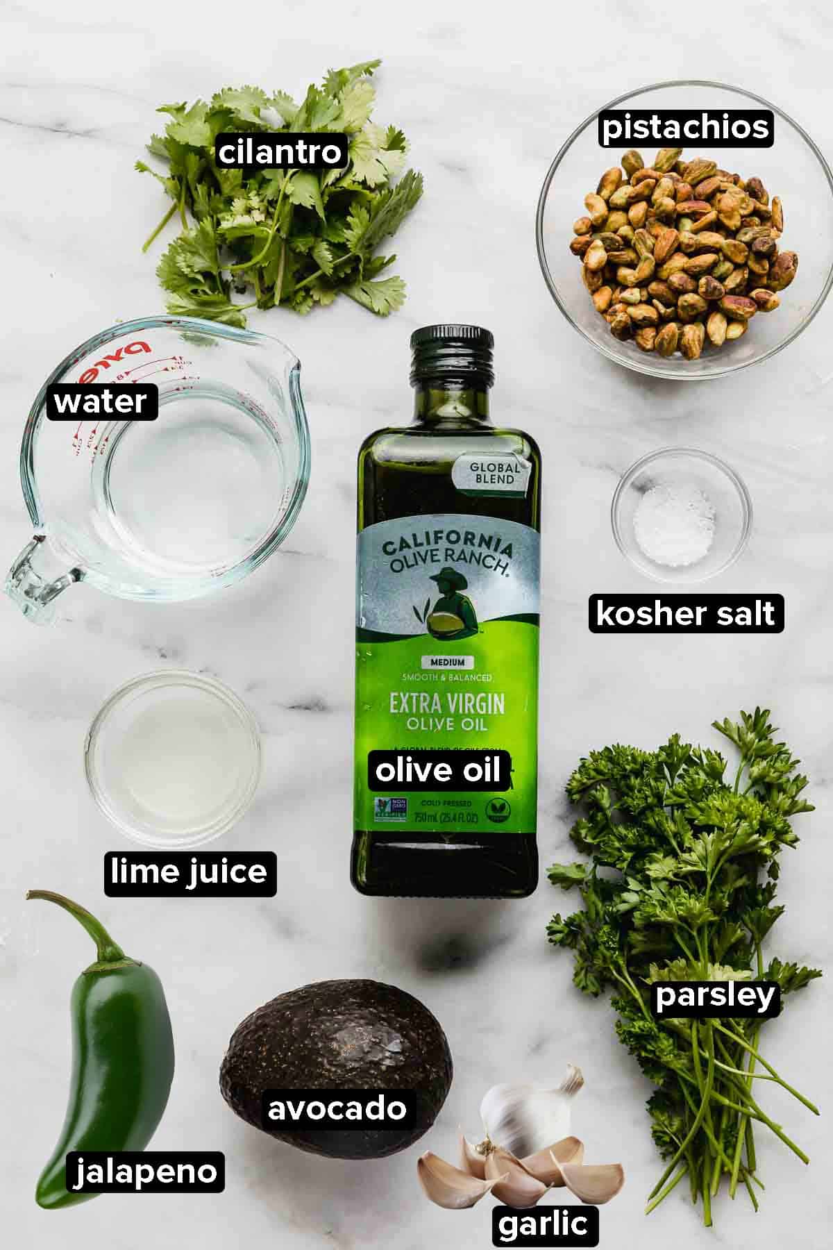 Green Sauce Recipe ingredients on a white background: parsley, cilantro, avocado, jalapeño, garlic, pistachios, and olive oil.