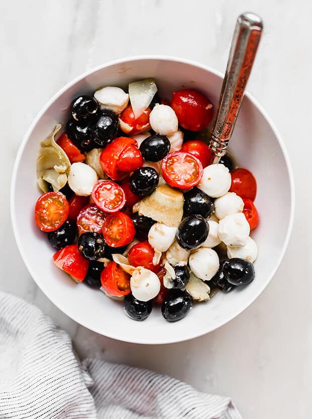 A white bowl with olives, mozzarella balls, tomatoes, and artichokes.