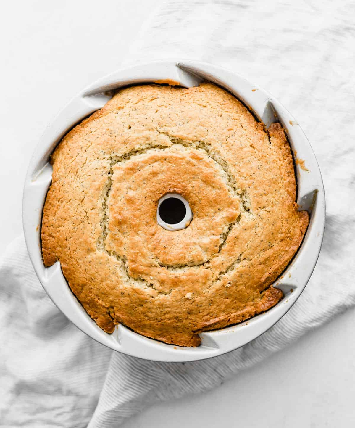 A baked Lemon Poppy Seed cake in a bundt pan on a white background.