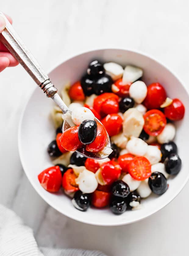 Tomatoes, an olive, and mozzarella ball on a spoon.