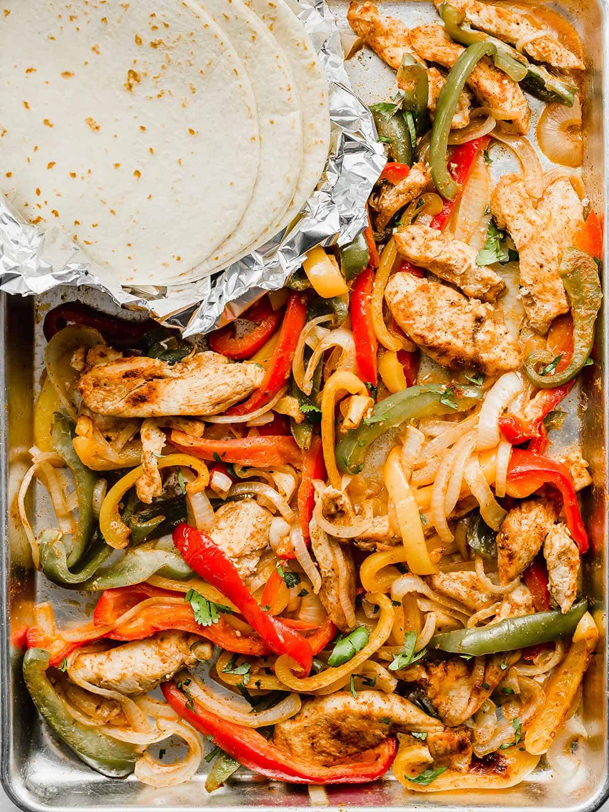 A baking sheet with cooked sliced peppers, chicken, and onions on it.