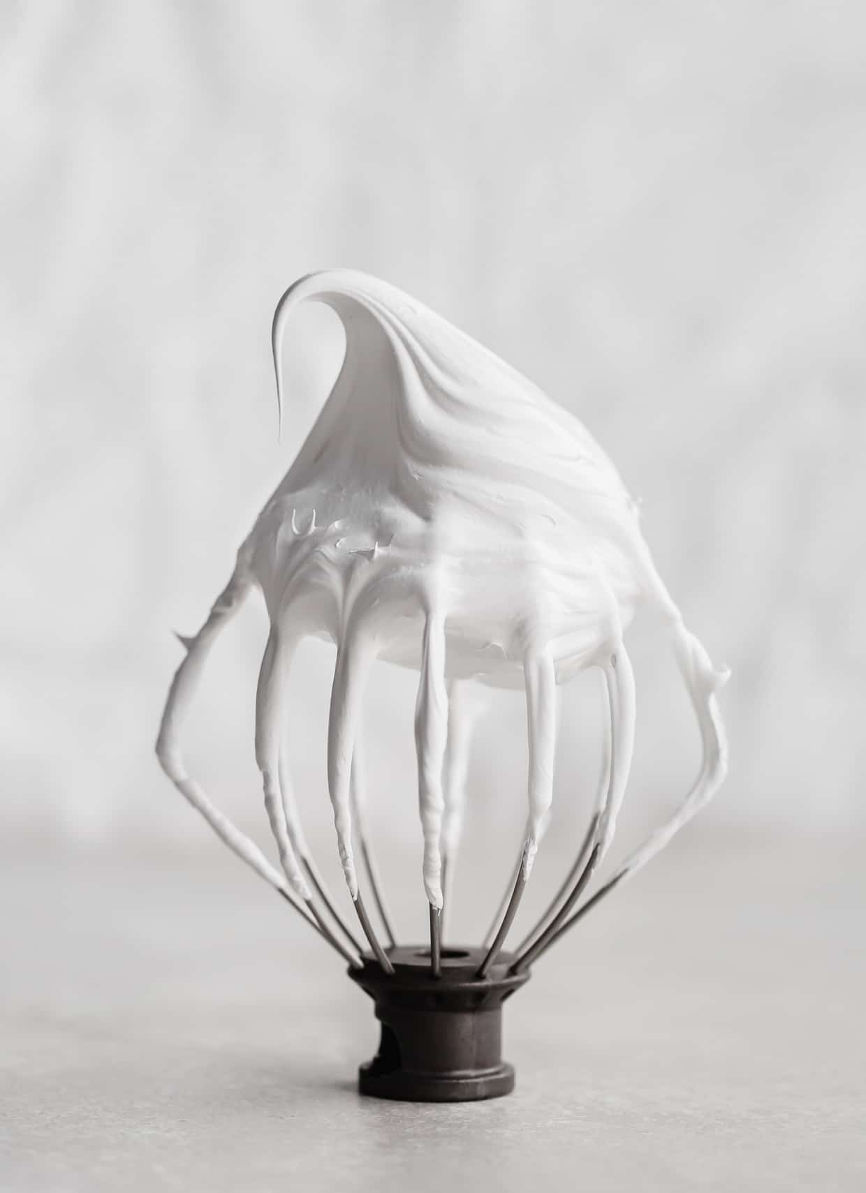 A whisk attachment with a billowy white Swiss meringue on it.