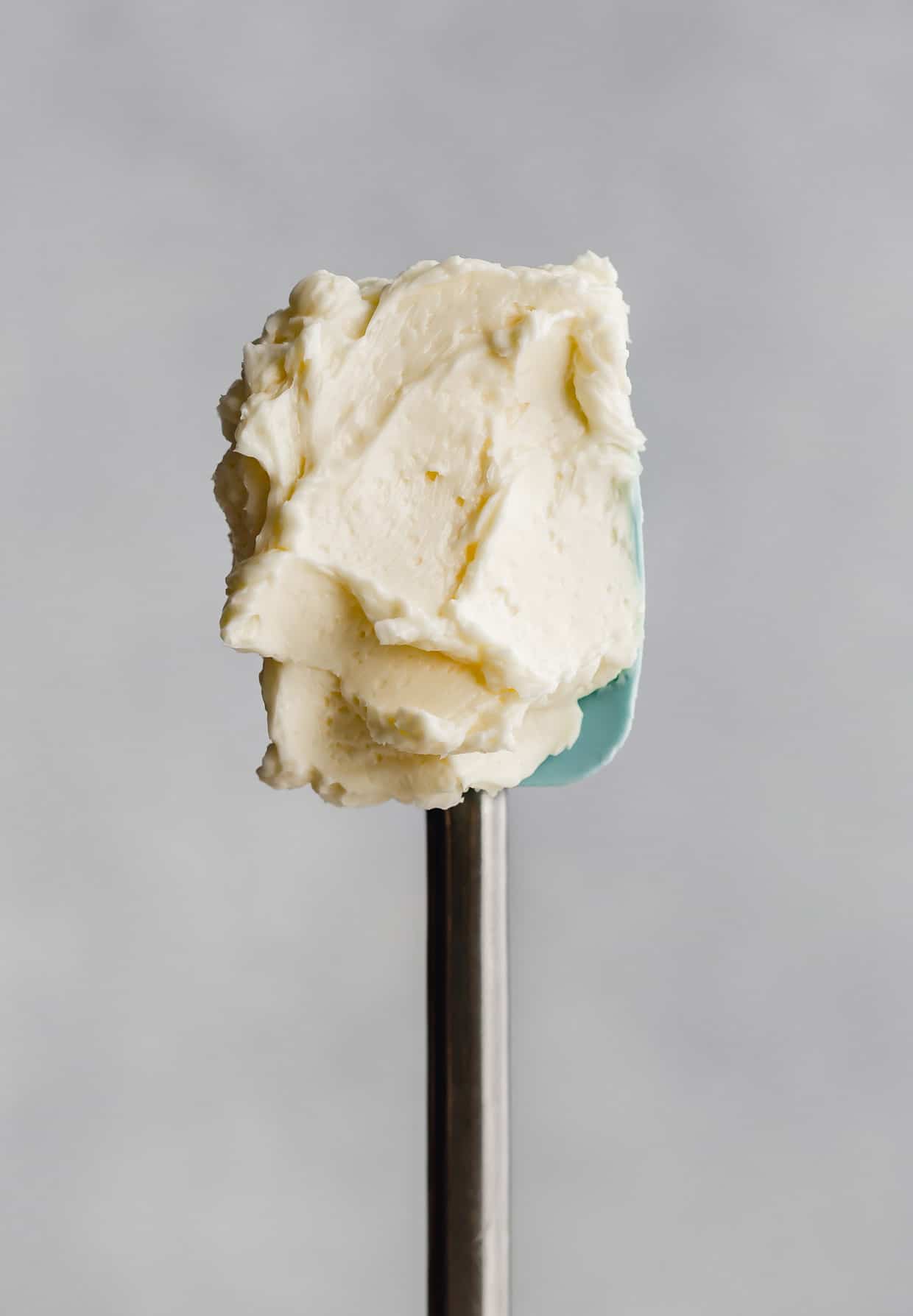 A teal rubber spatula with Swiss Meringue Buttercream on it.