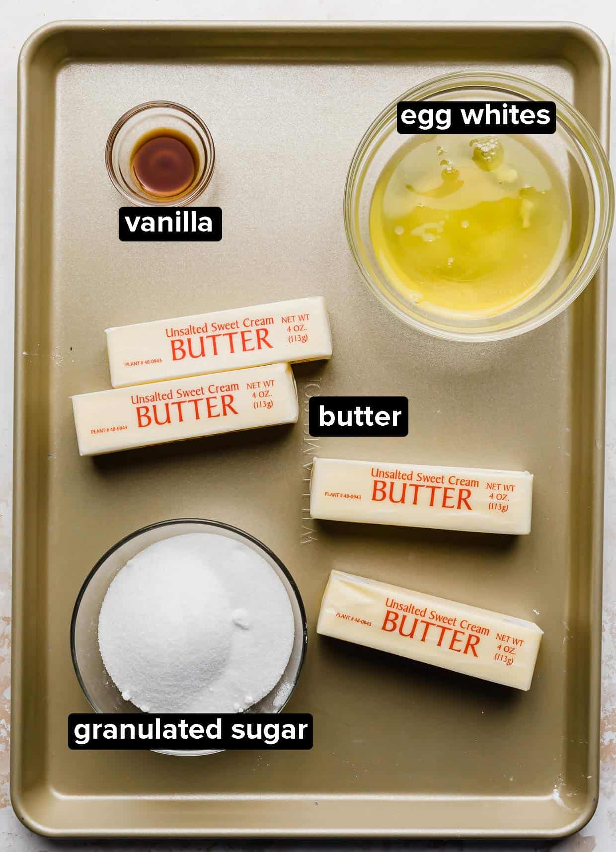 Swiss Meringue Buttercream ingredients on a bronze baking sheet: butter, egg whites, sugar, and vanilla.
