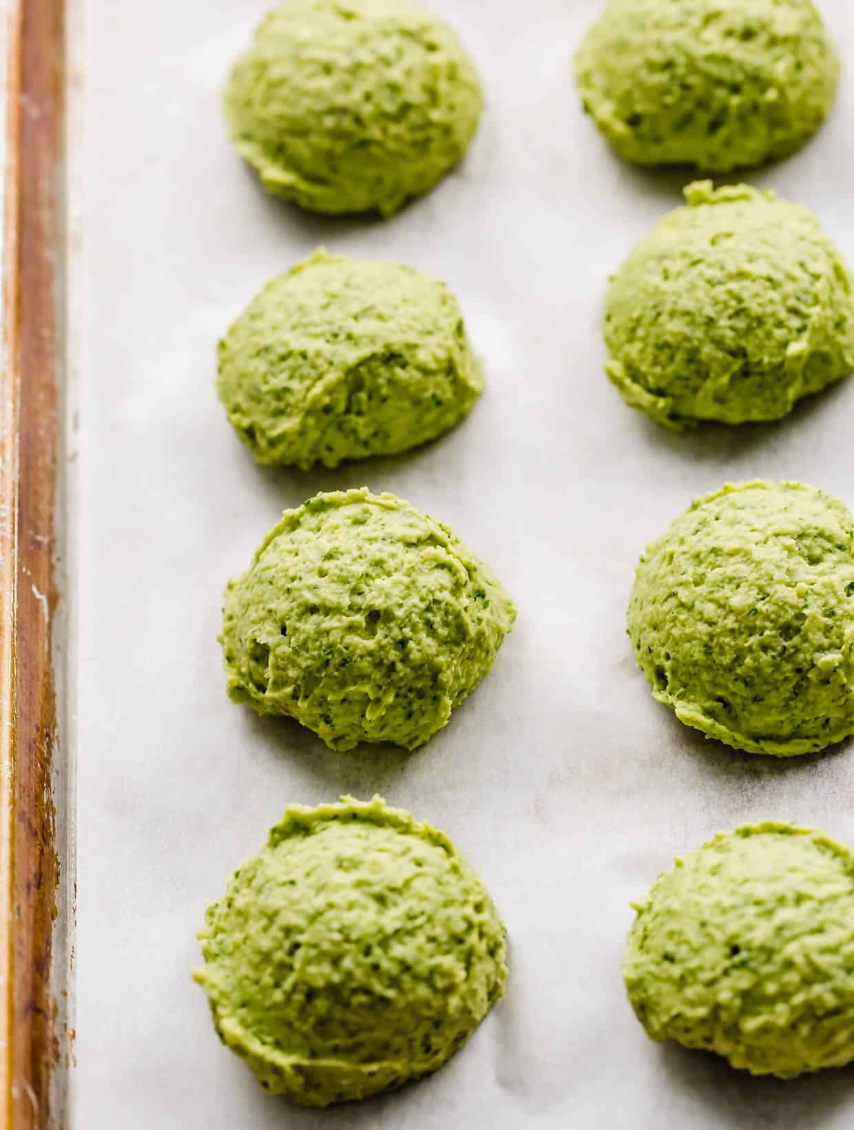 Unbaked green falafel rounds on a white parchment lined baking sheet.