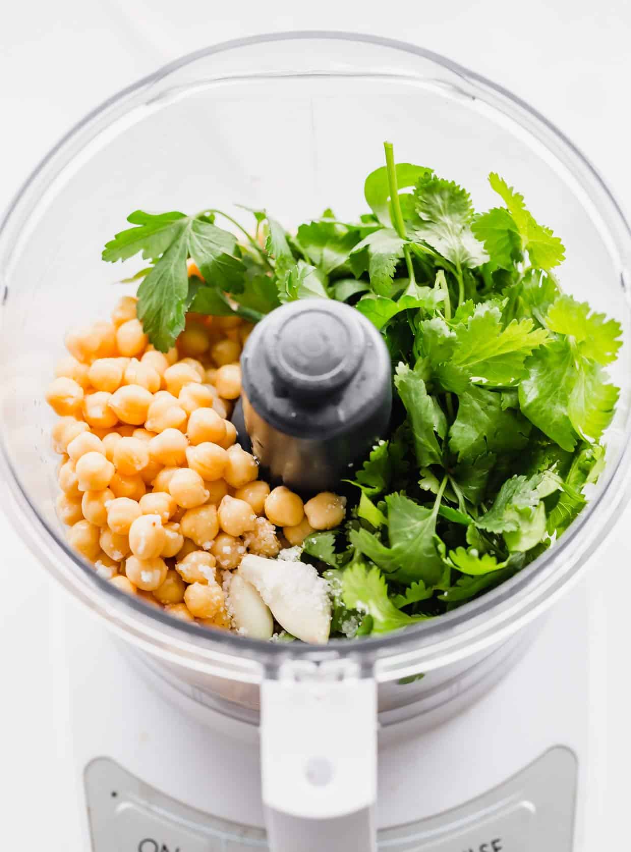 Food processor with chickpeas, fresh parsley in it.