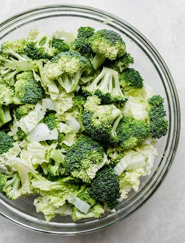 Broccoli florets and thinly sliced Napa cabbage in a glass bowl.