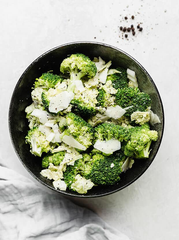 Overhead photo of broccoli Caesar salad in a black bowl against a white background.