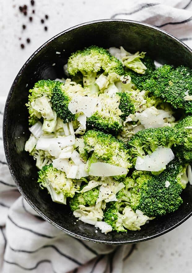A close up photo of a broccoli Caesar salad in a black bowl.