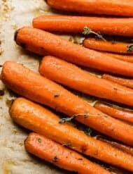 A close up photo of Brown Sugar Roasted Carrots on a tan parchment paper.