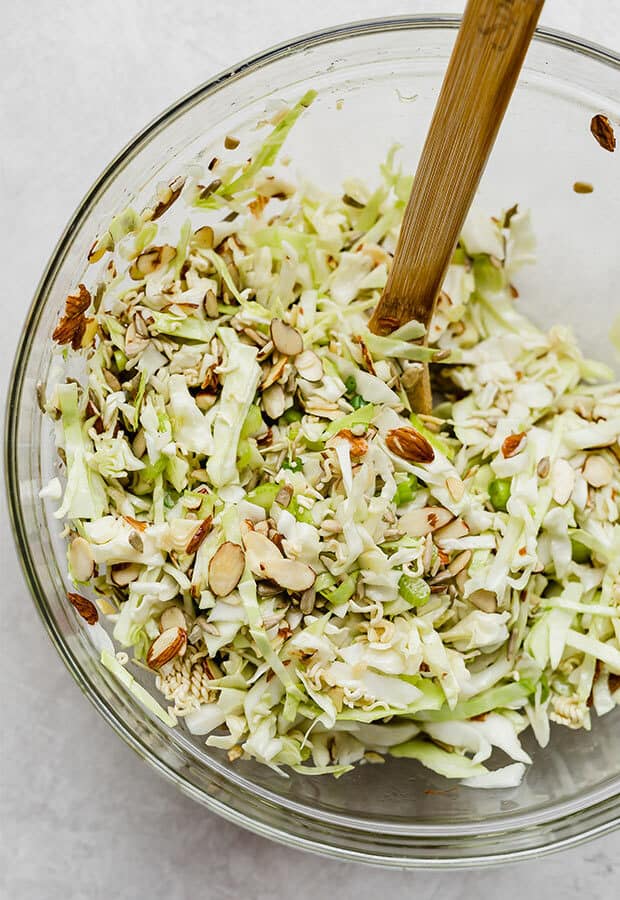 A wooden spoon stirring cabbage salad in a large bowl.