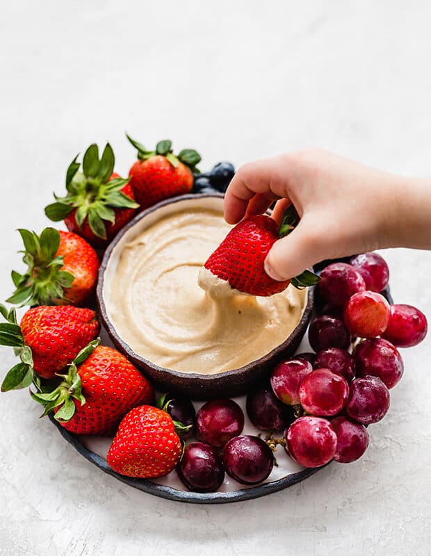 A strawberry being dipped into some cream cheese fruit dip.