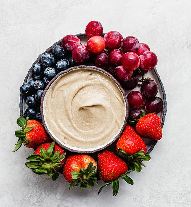 A bowl of fruit dip surrounded by fresh berries.