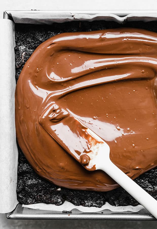A spatula spreading melted chocolate over brownies.