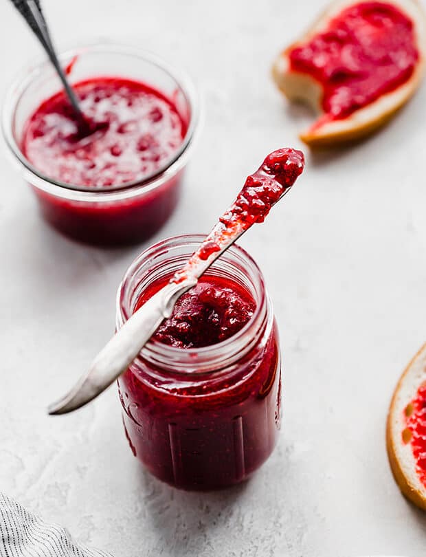 A knife covered in raspberry jam, resting on a glass jar.