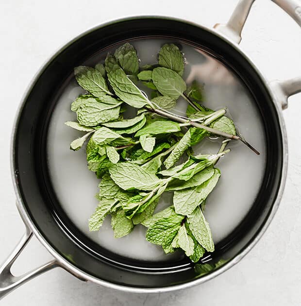 A saucepan with sugar, water, and mint leaves.