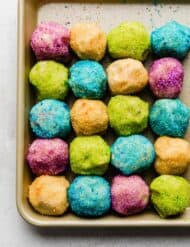 Sugar cookie dough balls covered in green, purple, yellow, and blue colored sugar.