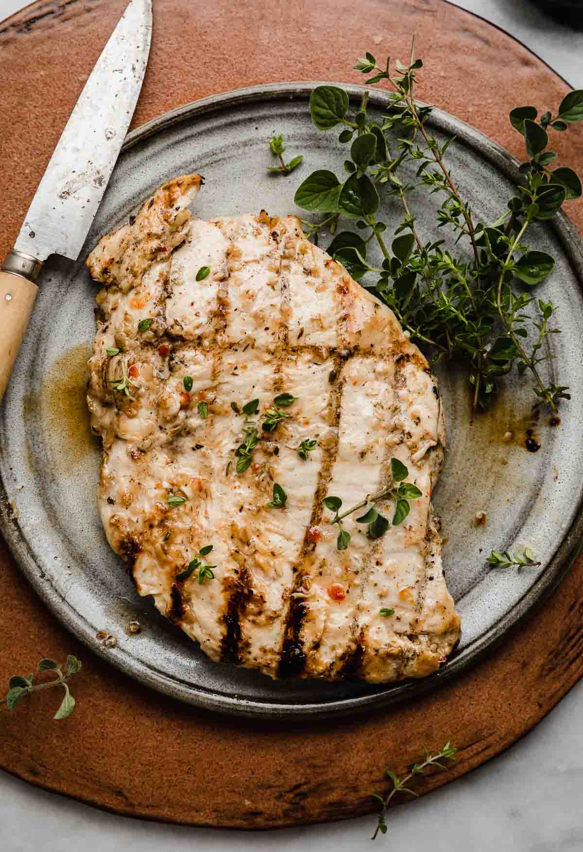 A grilled chicken that was marinated in an Italian chicken marinade, on a gray plate on a brown background.