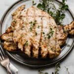 Italian Grilled Chicken surrounded by fresh herbs, on a gray plate.